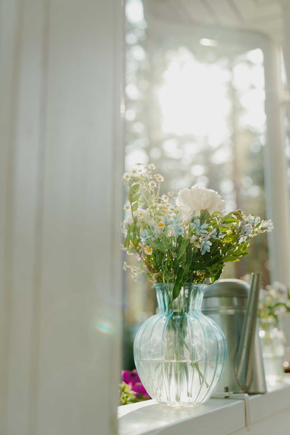 Vase en verre avec des fleurs et devant une fenêtre